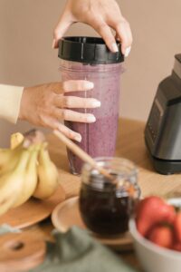 Person blending fresh fruit smoothie in a container with a lid next to bananas and honey.