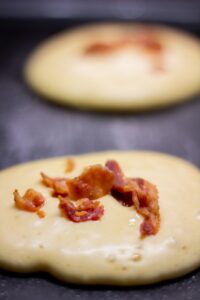 Pancakes with bacon are being cooked. Griddle