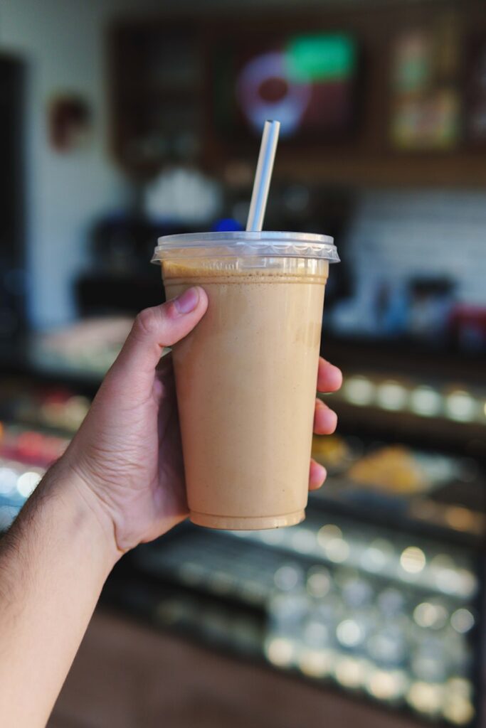 a hand holding a cup with a straw in it iced coffee, neoprene cup sleeves, insulated cup sleeve