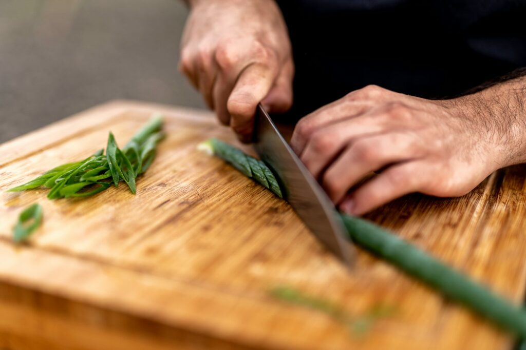 a person cutting up some green leaves on a cutting board